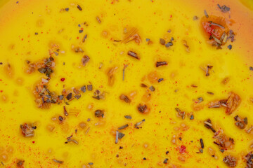 Close up of yellow plastic plate with herbs and spices and pieces of vegetables in sauce or...