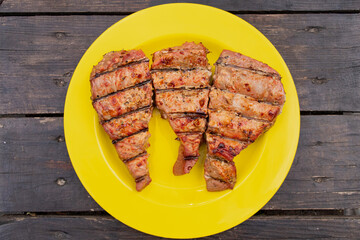 Three tuna steaks cooked on the grill with a crispy crust and cuts and lying on a plastic yellow plate on a wooden table