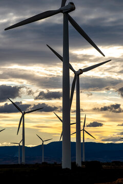 Wind turbines at sunset in Zaragoza Spain, silhouettes against dramatic sky, symbolizing renewable energy, green technology and sustainable environmental progress