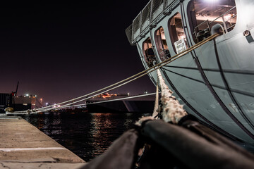Middle East, Middle East - 18 December 2023: View of docked vessels illuminated against the dark waters, their steel hulls reflecting the city's faint glow, secured by thick ropes in the quiet harbor.