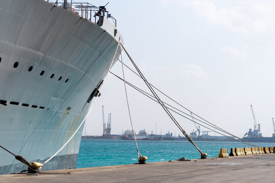 Middle East, Middle East - 22 December 2023: View of the colossal ship's hull against the bright turquoise sea, a stark contrast to the distant port's industrial cranes.