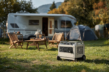 Portable generator powering a campsite with camper van, tent, and table with chairs, ensuring power supply during outdoor adventures