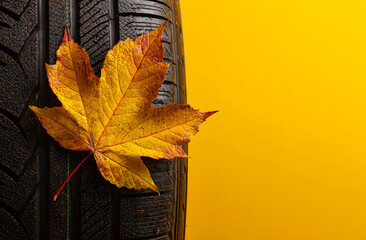 autumn leaf resting on a car tire against yellow background closeup symbolizing seasonal change and fall driving safety perfect for automotive advertising and autumn promotion visuals
