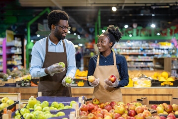 Staff working together arranging apples in a grocery store produce section