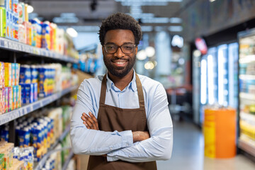 Smiling employee in grocery store aisle wearing apron while standing confidently
