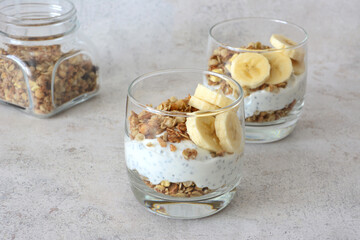 Yogurt parfait in glasses with granola and banana slices on gray background
