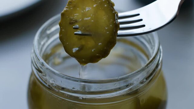 A pickle slice is lifted from brine, dripping slowly with rich texture and refreshing detail