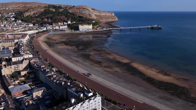 Aerial video of Llandudno Pier stretching into the sea beside the cliffs of the Great Orme on a summer day. 