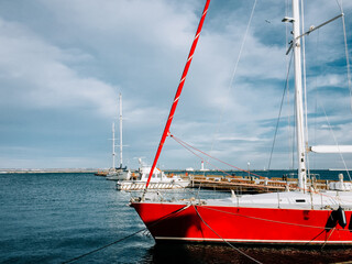 Sailboats docked at a marina with clear skies and calm waters under bright sunlight