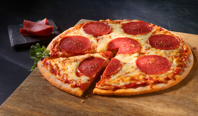 Pizza mit Salami und Kaese mit Oregano auf rustikaler Holzplatte, Pizza, Italien, Slice, 