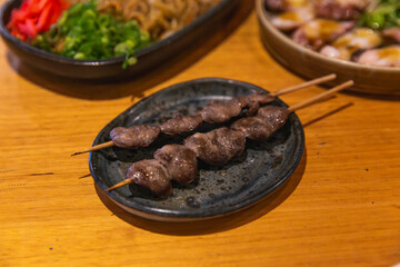 Grilled Japanese chicken hearts on skewers served on a dark ceramic plate, traditional yakitori style with rich umami glaze