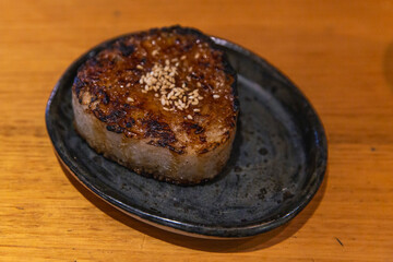 Japanese grilled rice ball with a crispy soy glaze crust and white sesame topping served on a dark rustic plate, close-up view