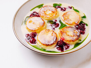Homemade cottage cheese pancakes (syrniki) served with creamy sauce, berry topping, and fresh garnish on a plate, traditional Eastern European dessert breakfast.