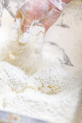 Raw chicken piece coated in thick seasoned flour being lifted by gloved hand, step in fried chicken preparation showing texture and coating
