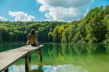 Frau sitzt auf einem Steg am See beim Jezioro Szmaragdowe, Smaragdsee, in Stettin (Szczecin), Polen © Jan Wagner