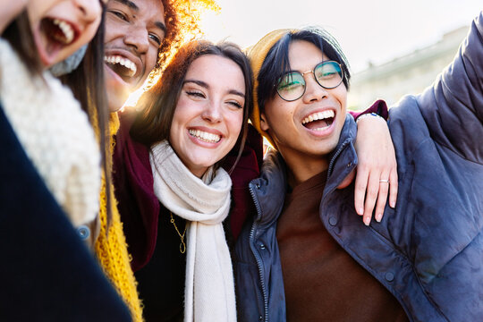 Diverse group of young friends having fun together outdoors on winter. Millennial student people laughing walking in city street enjoying day off. Youth community and friendship concept.