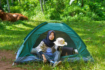 Portrait of young Asian woman camping with small tent for solo camping in forest, with nature and cow background