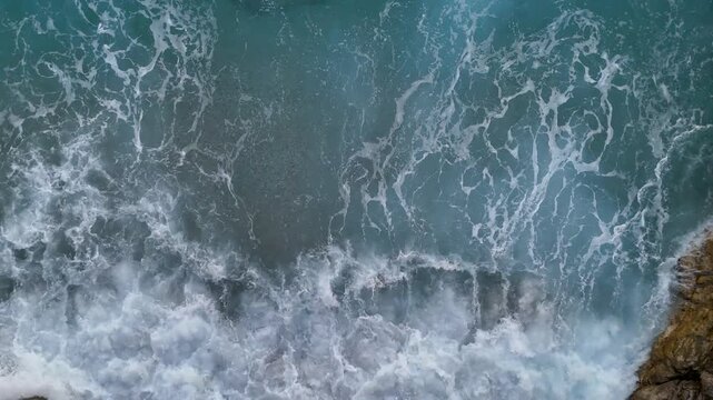 A mesmerizing 4K top-down aerial view of a deep blue sea with turbulent white waves creating a powerful and beautiful abstract natural background of the ocean's raw energy