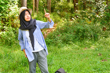Sporty Muslim Asian woman standing near tent and backpack, enjoying sunny afternoon in the mountains. Camping lifestyle concept