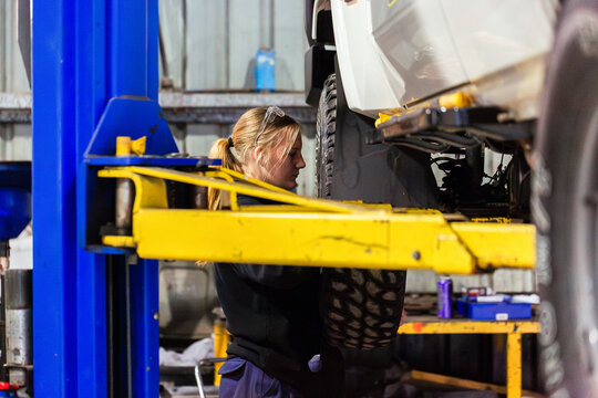 Female mechanic working on vehicles underbody inside workshop