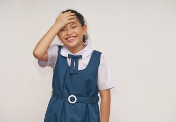 Portrait of an Asian student in a school uniform, a preteen girl aged 8-9 years old, happy emotion through a smiling face, hand touching forehead, studio shot.