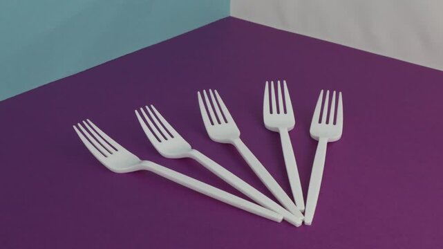 Plastic cutlery in a circle shape on a purple background and an abstract composition copy space, and a conceptual art still life