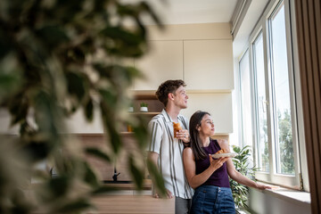Young couple enjoying breakfast and looking out window in modern kitchen