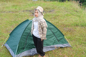 Sporty Muslim Asian woman standing near tent and backpack, enjoying sunny afternoon in the mountains. Camping lifestyle concept