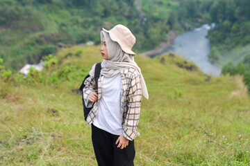 Sporty Muslim Asian woman standing near tent and backpack, enjoying sunny afternoon in the mountains. Camping lifestyle concept