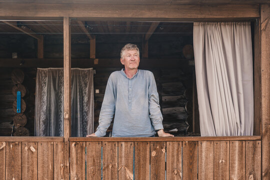 handsome man middle aged stands relaxed on wooden balcony, taking in serene surroundings rustic cabin. sunlight filters in, creating calm atmosphere in nature. close up.