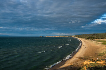 beautiful, serene beach extends along coast, where soft waves meet golden sand under moody sky filled with clouds, inviting leisure and exploration at dusk.
