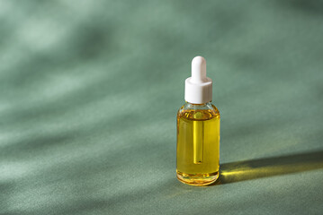 Cosmetic serum in glass dropper bottle on green background with sunlight and shadows