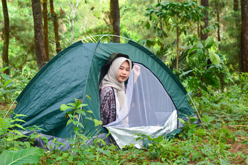 Sporty Muslim Asian woman standing near tent and backpack, enjoying sunny afternoon in the mountains. Camping lifestyle concept