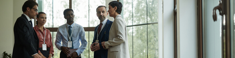 Header of group of middle aged multiethnic professionals standing together discussing business strategy in modern office setting, including Caucasian man, Black man, Caucasian woman