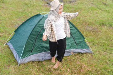 Sporty Muslim Asian woman standing near tent and backpack, enjoying sunny afternoon in the mountains. Camping lifestyle concept