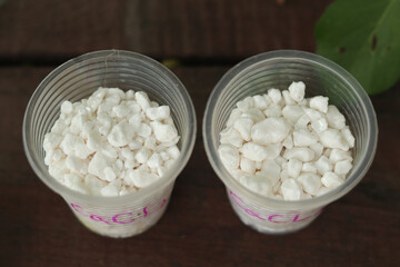 Large white granules of calcium chloride of mineral origin in two plastic cups. Used as an additive for concrete, in medicine and as a food additive.