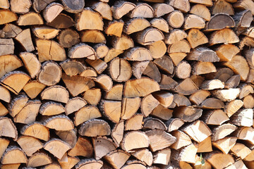 Firewood stacked in a pile along the wall. Cut wooden logs. Firewood stored along the wall in the yard on the street. Fuel for the stove in winter. Firewood is stacked for drying