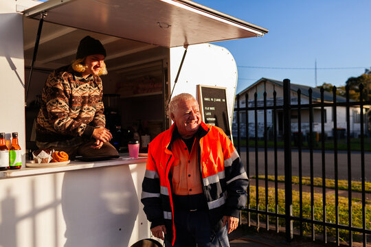 happy older Aussie workman in high vis workwear buying warm takeaway coffee from van