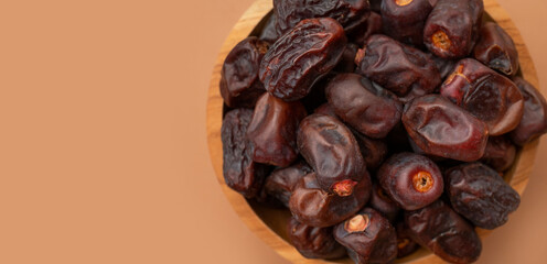 Delicious dried dates in wooden bowl on brown background flat lay top view. Oriental fruit, date palm fruit, natural sweet dessert. Organic healthy snack, food background