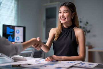Fototapeta premium Businesswomen shaking hands after successful meeting using charts and graphs on computer