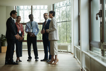 Group of middle aged and young professionals including Caucasian man, woman, Black man, and multiethnic colleagues standing in office discussing business strategy