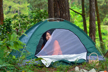 Sporty Muslim Asian woman standing near tent and backpack, enjoying sunny afternoon in the mountains. Camping lifestyle concept