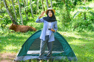 Sporty Muslim Asian woman standing near tent and backpack, enjoying sunny afternoon in the mountains. Camping lifestyle concept