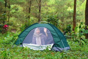 Sporty Muslim Asian woman standing near tent and backpack, enjoying sunny afternoon in the mountains. Camping lifestyle concept