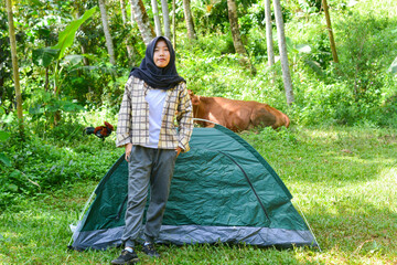 Sporty Muslim Asian woman standing near tent and backpack, enjoying sunny afternoon in the mountains. Camping lifestyle concept