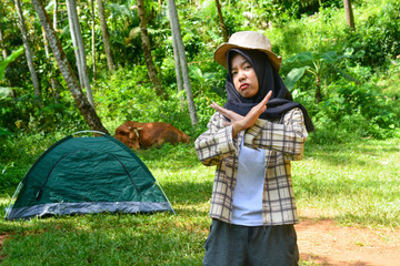 Sporty Muslim Asian woman standing near tent and backpack, enjoying sunny afternoon in the mountains. Camping lifestyle concept