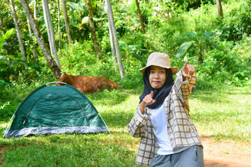 Sporty Muslim Asian woman standing near tent and backpack, enjoying sunny afternoon in the mountains. Camping lifestyle concept