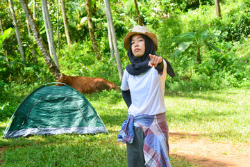 Sporty Muslim Asian woman standing near tent and backpack, enjoying sunny afternoon in the mountains. Camping lifestyle concept