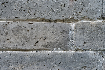 Close up texture of a weathered grey stone wall with rough surfaces and visible mortar lines showing age and natural elements
