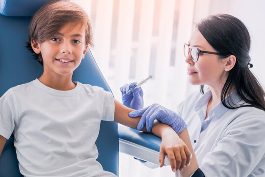 Female doctor pediatrician injecting vaccine to little boy in medical clinic for receiving anti-bodies, immunization boost. Vaccination against coronavirus, hepatitis, flu, measles, chicken pox